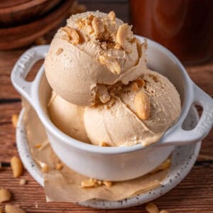 Scoops of peanut butter ice cream in a bowl with peanuts on top showing the creamy texture.
