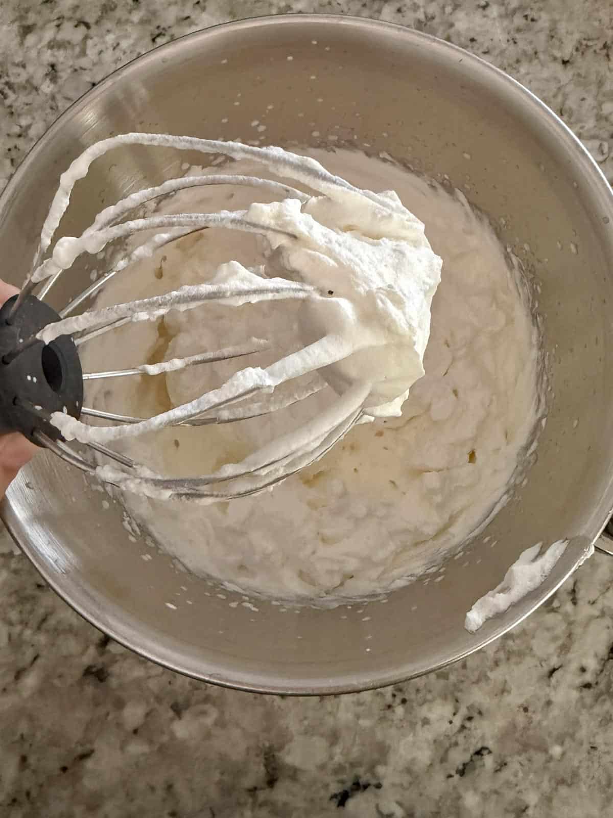 Heavy cream whipped until stiff peaks showing the peaks on the whisk attachment.
