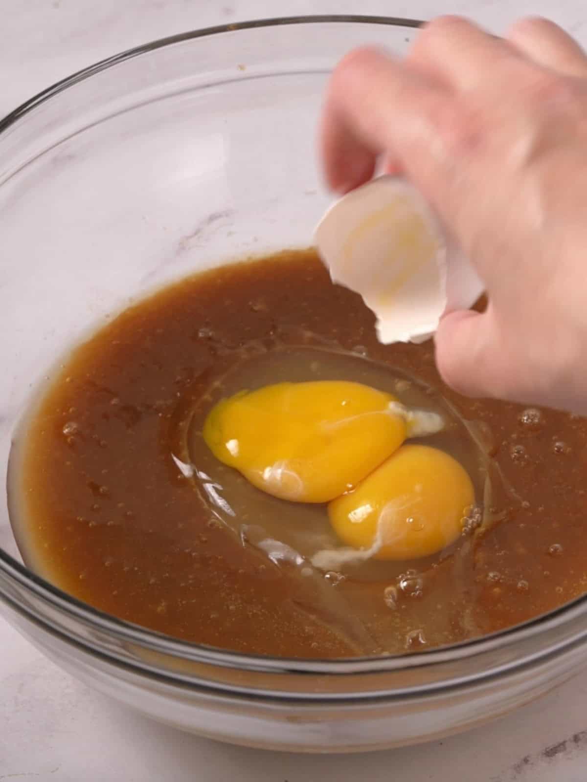 Egg and egg yolk being added to the melted butter and sugars in a bowl.