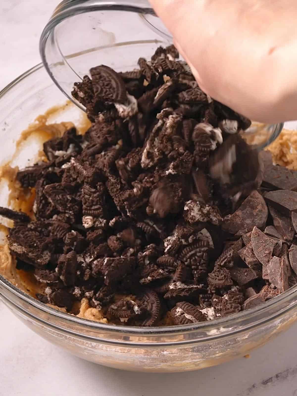 Chopped Oreos and chopped chocolate being added to the blondie batter in a bowl.