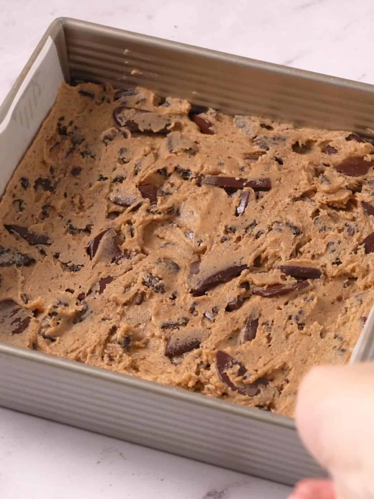 Oreo blondie batter spread out in a 8X8 inch metal baking pan.