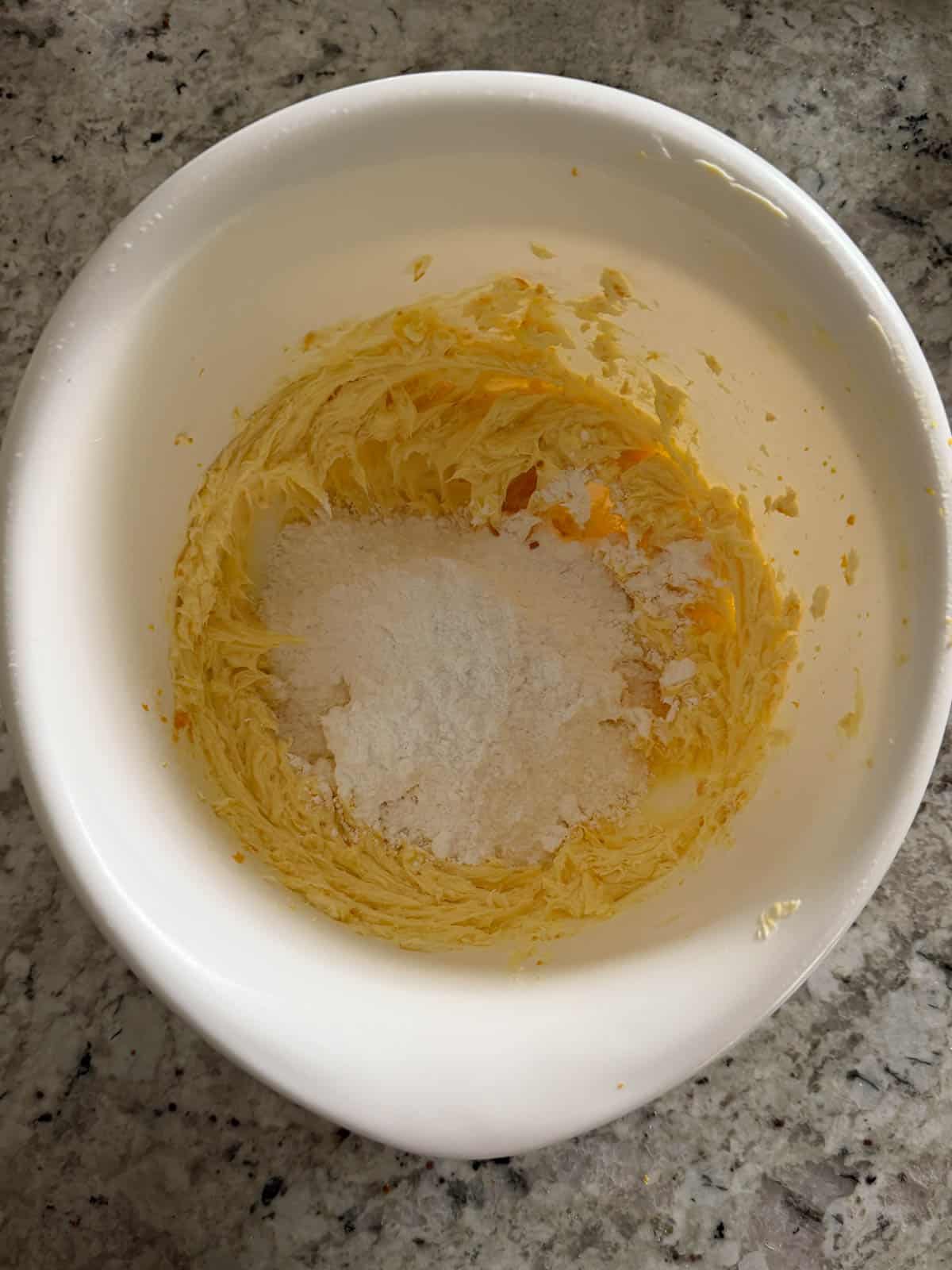 Powdered sugar being added to the butter in a white bowl on the counter.