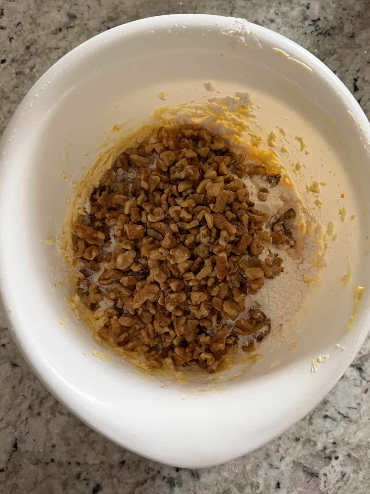 Chopped walnuts and flour being added to the cookie dough in a bowl on the counter.