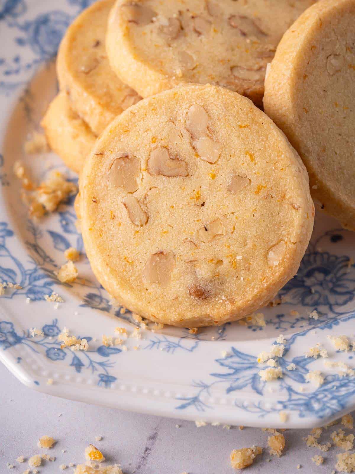 Shortbread cookies with walnuts on a plate with crumbs around it.