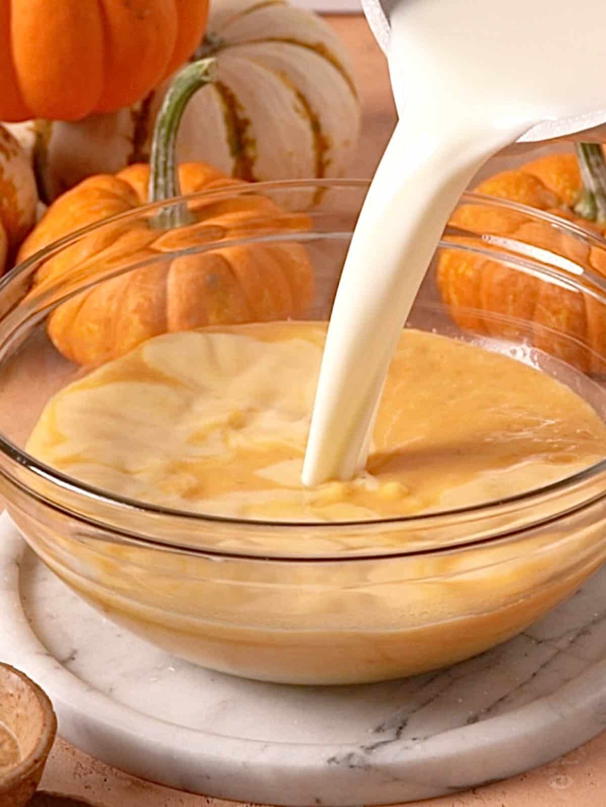Tempering the egg yolk mixture with the hot milk mixture in a bowl.