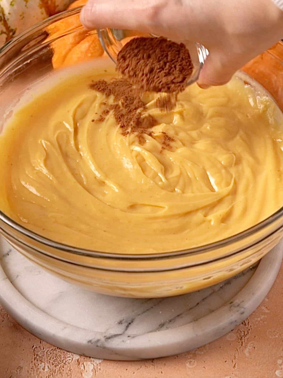 Adding pumpkin pie spice to the pastry cream in a glass bowl.