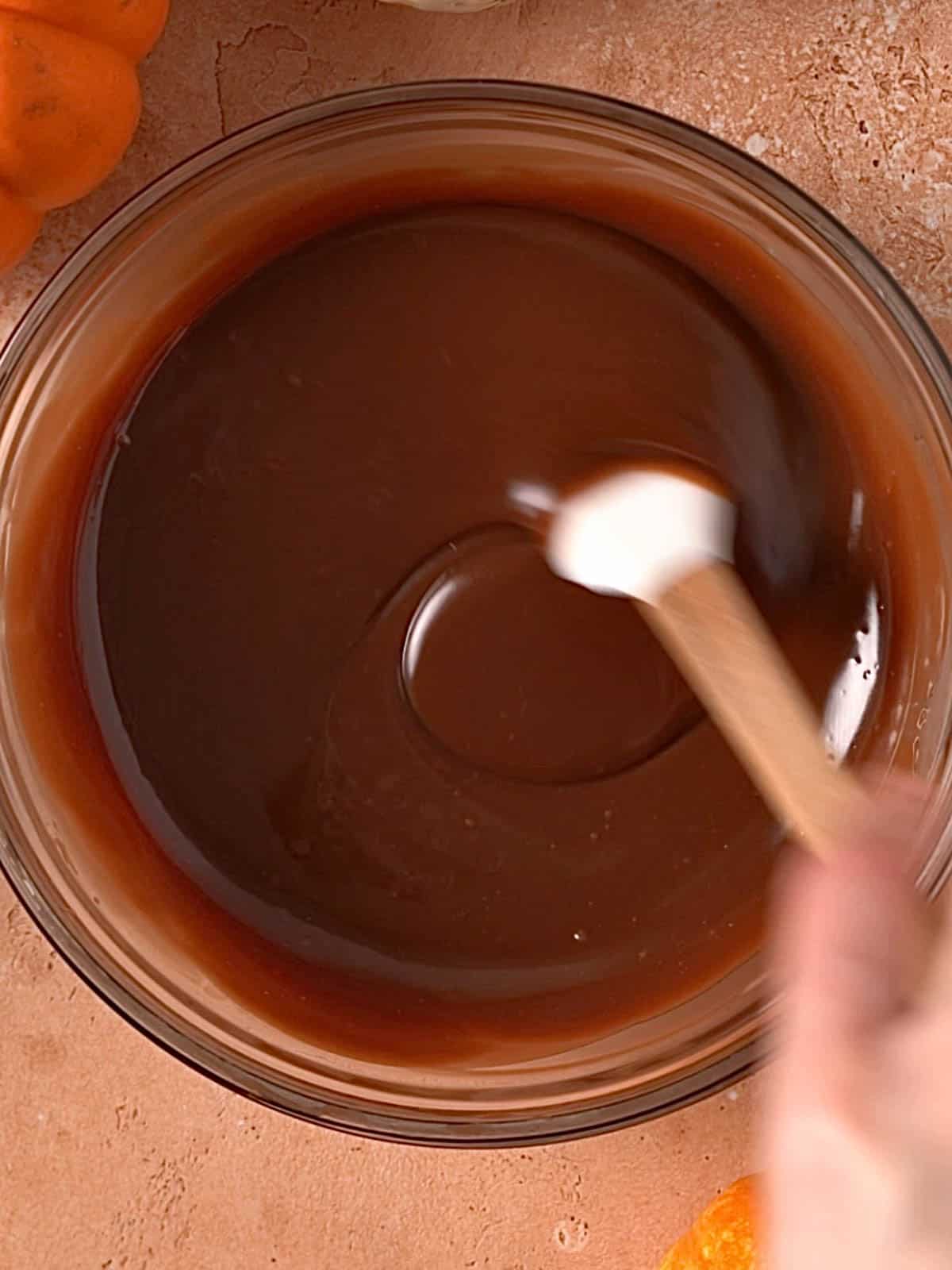 Milk chocolate ganache in a bowl being stirred with a spatula.