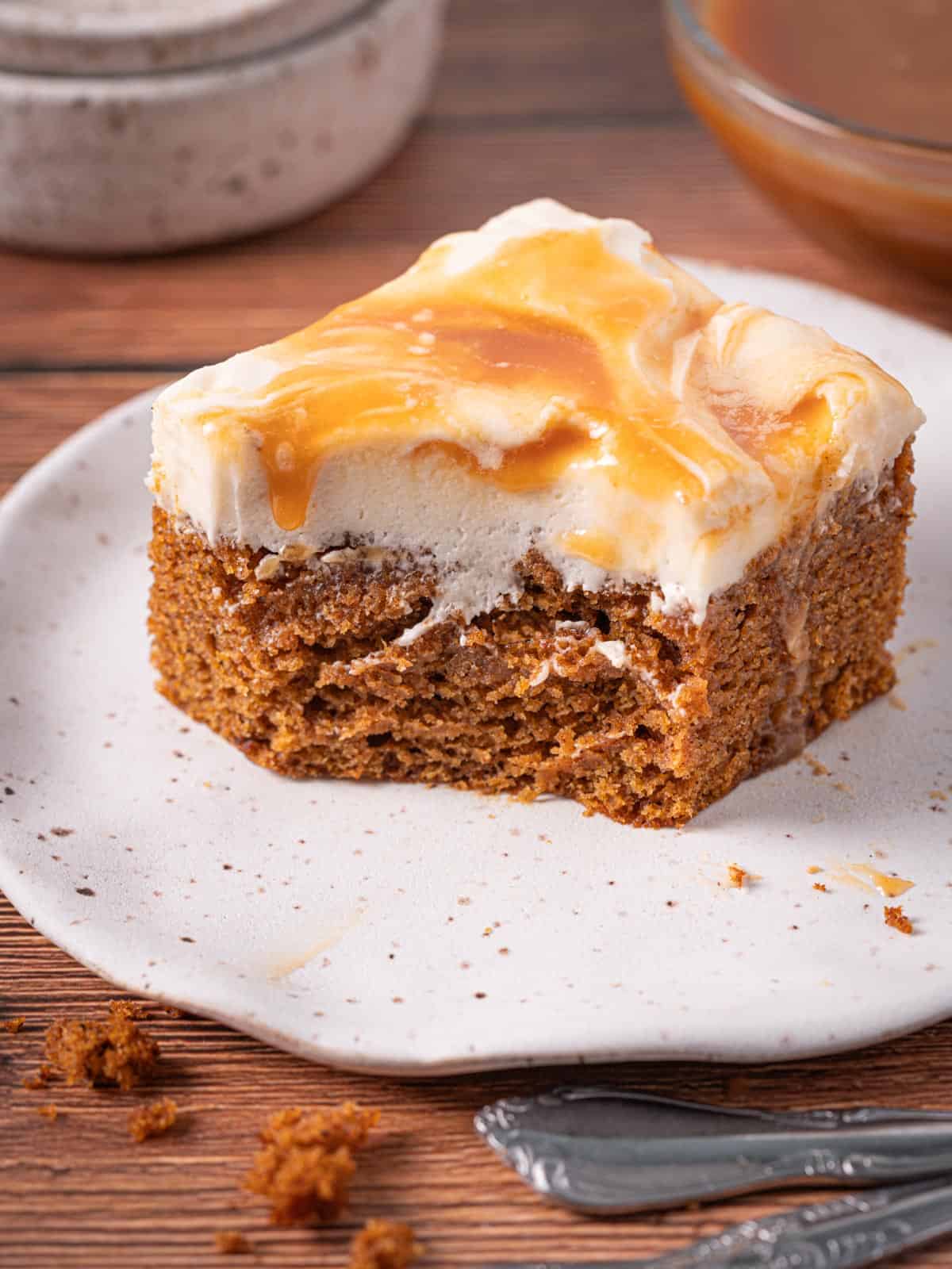 A slice of pumpkin cake with salted caramel cream cheese frosting on a plate with flaky sea salt.