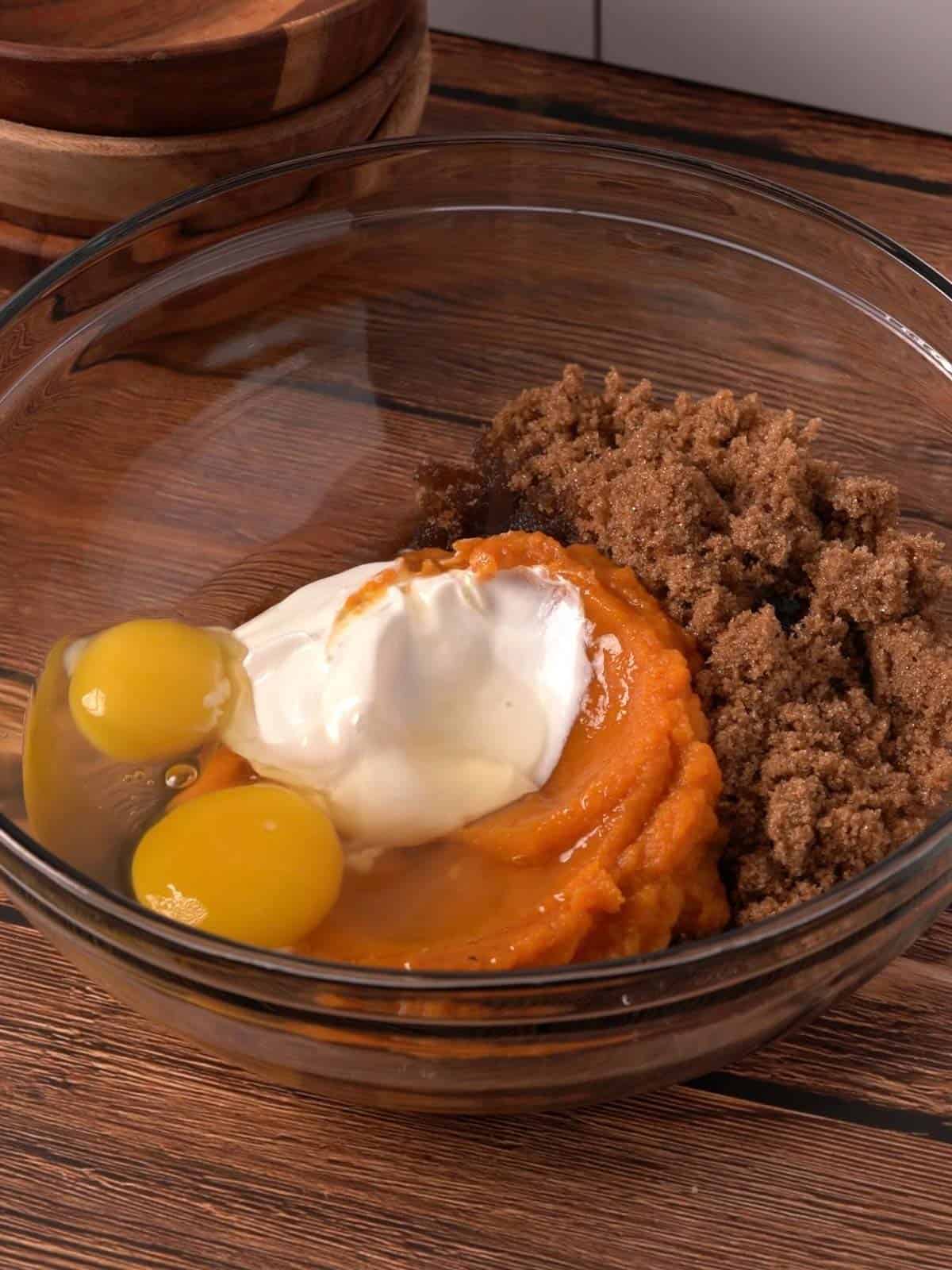 The eggs, pumpkin puree, brown sugar, sour cream, and oil in a glass bowl.