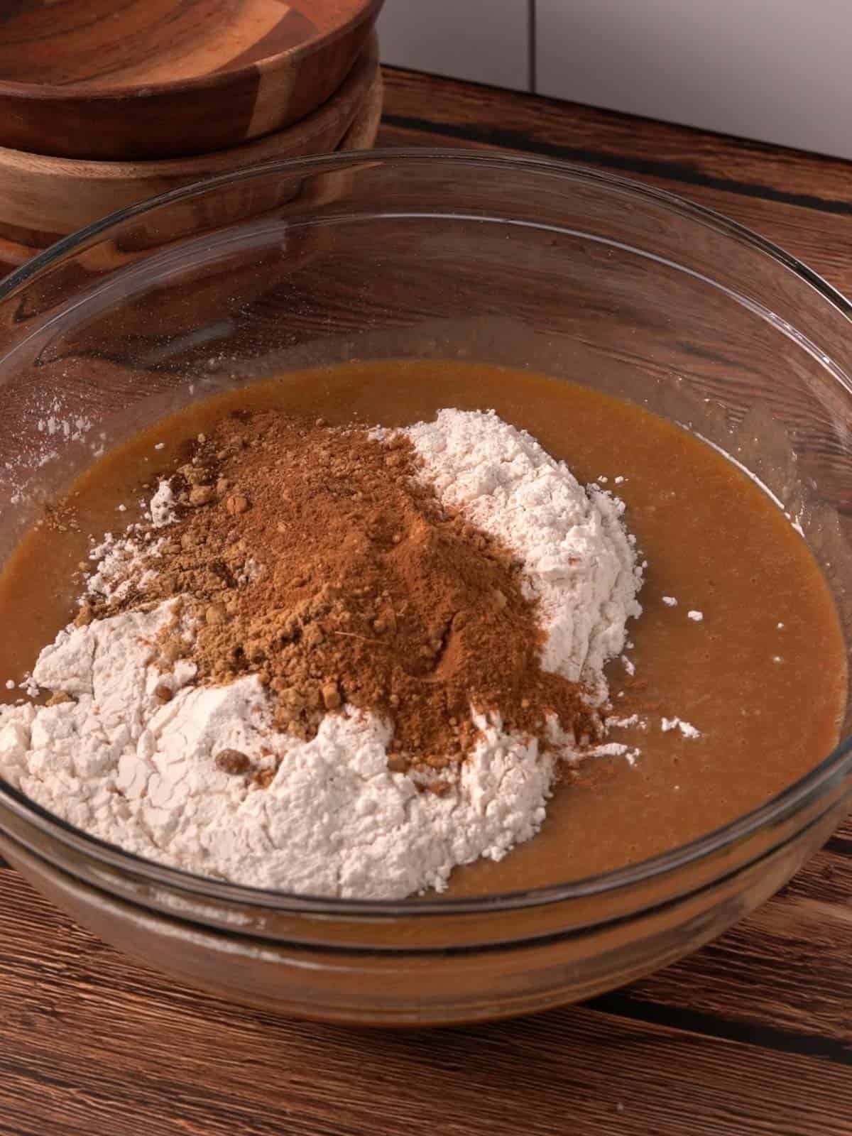 All purpose flour, baking soda, and spices being added to the wet ingredients in a glass bowl.