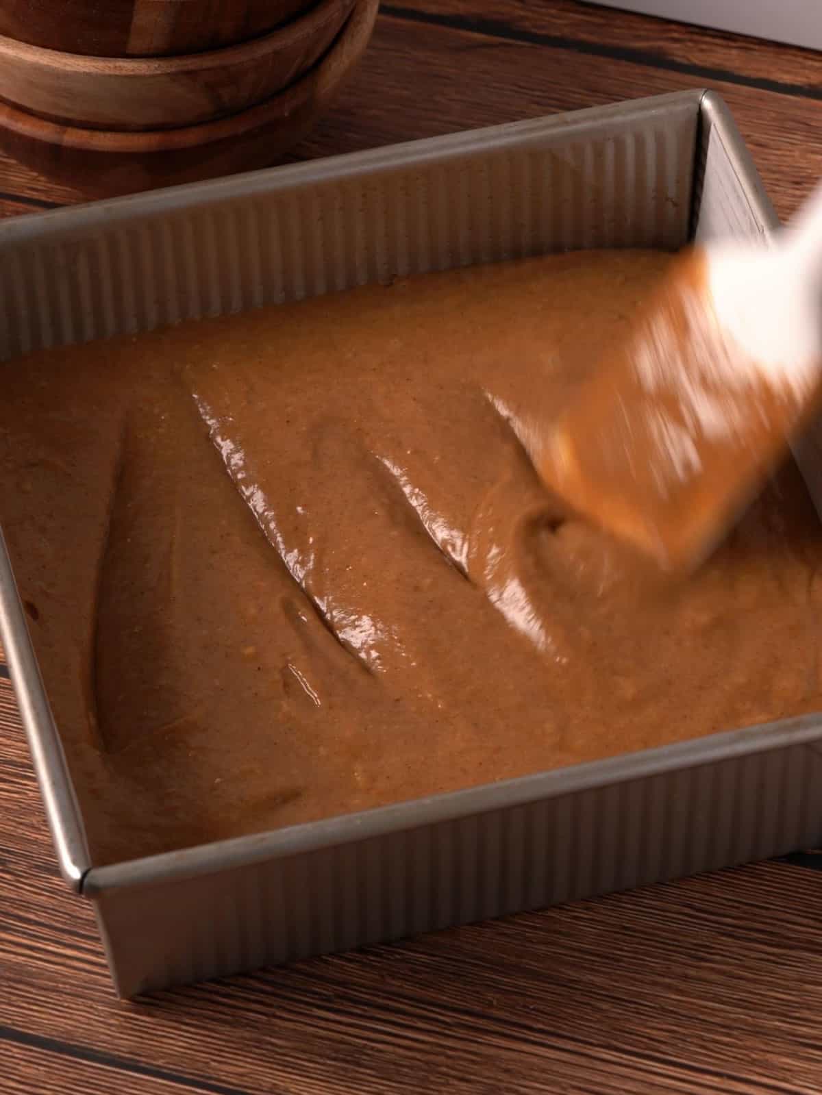 Spreading out the pumpkin cake batter in an 8X8 metal baking pan.