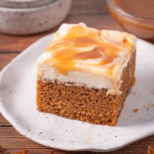 Moist caramel pumpkin cake slice with salted caramel cream cheese frosting on top with dripping caramel.