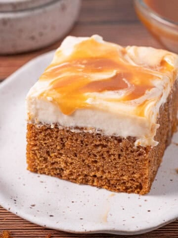 Moist caramel pumpkin cake slice with salted caramel cream cheese frosting on top with dripping caramel.